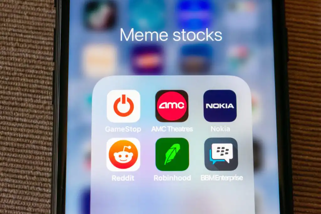 A smartphone screen displays a folder labeled “Meme stocks,” containing icons for GameStop, AMC Theatres, Nokia, Reddit, Robinhood, and BBM Enterprise apps. The background is blurred.