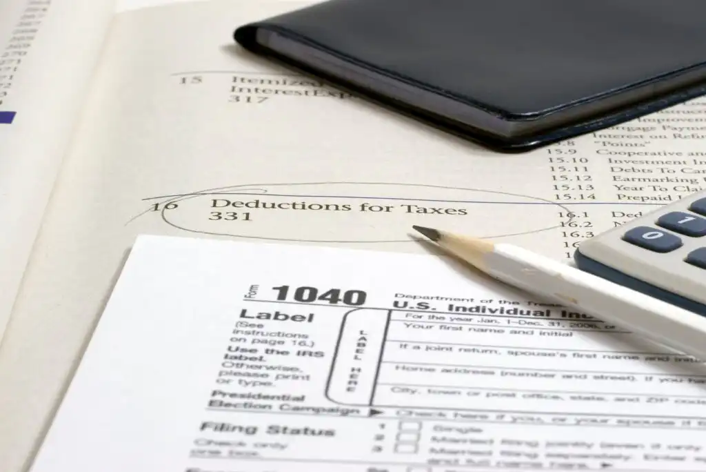 A tax form 1040, a pencil, and a calculator resting on a document with “Deductions for Taxes” circled. A black wallet is also visible at the top of the image.