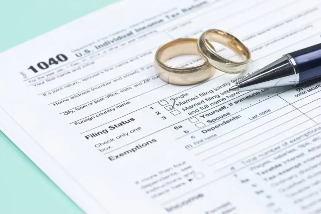 Two gold wedding rings and a pen rest on a US 1040 tax form, with the Married filing jointly filing status box checked.
