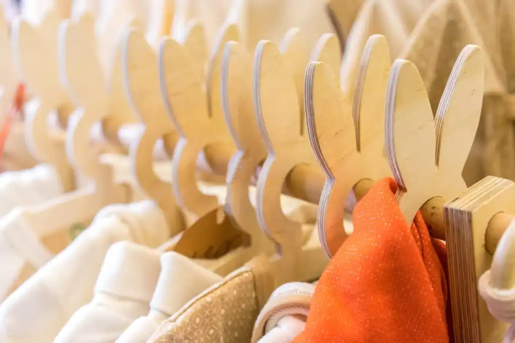 A row of wooden hangers shaped like bunny ears holds light-colored and orange clothing items in a closet.
