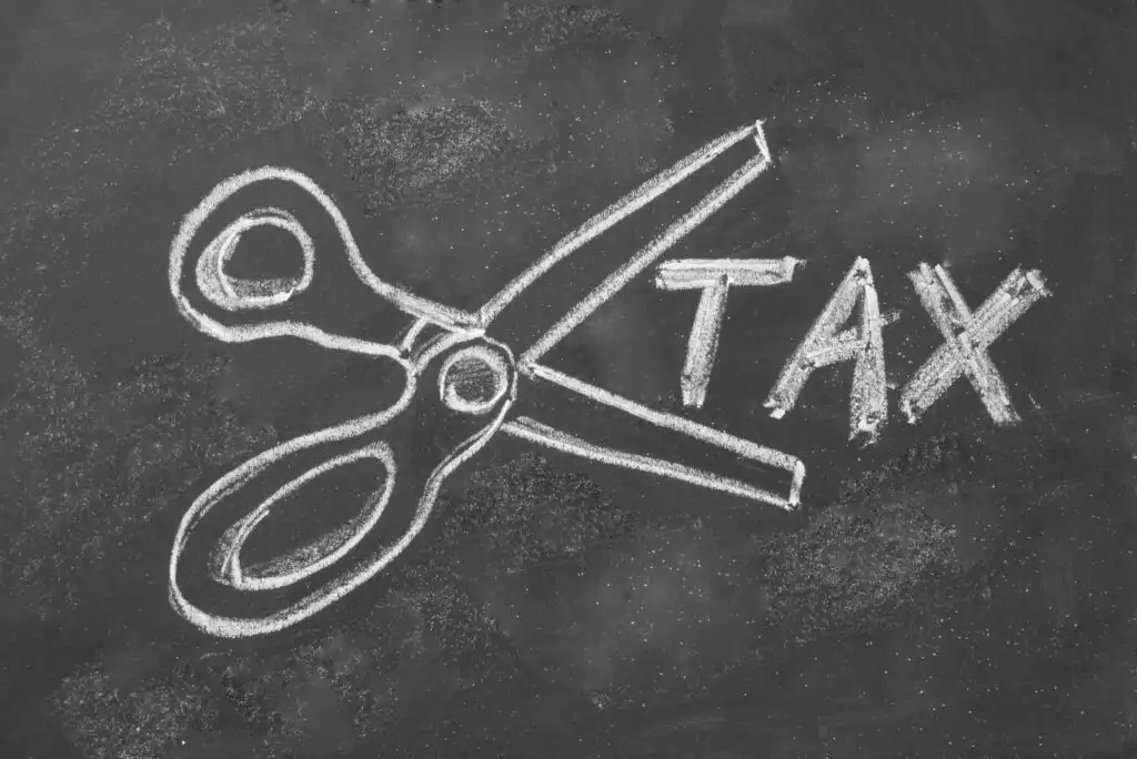 A drawing of open scissors on a chalkboard appears to cut through the word TAX, which is written in large letters, suggesting the concept of tax cuts or tax reduction.