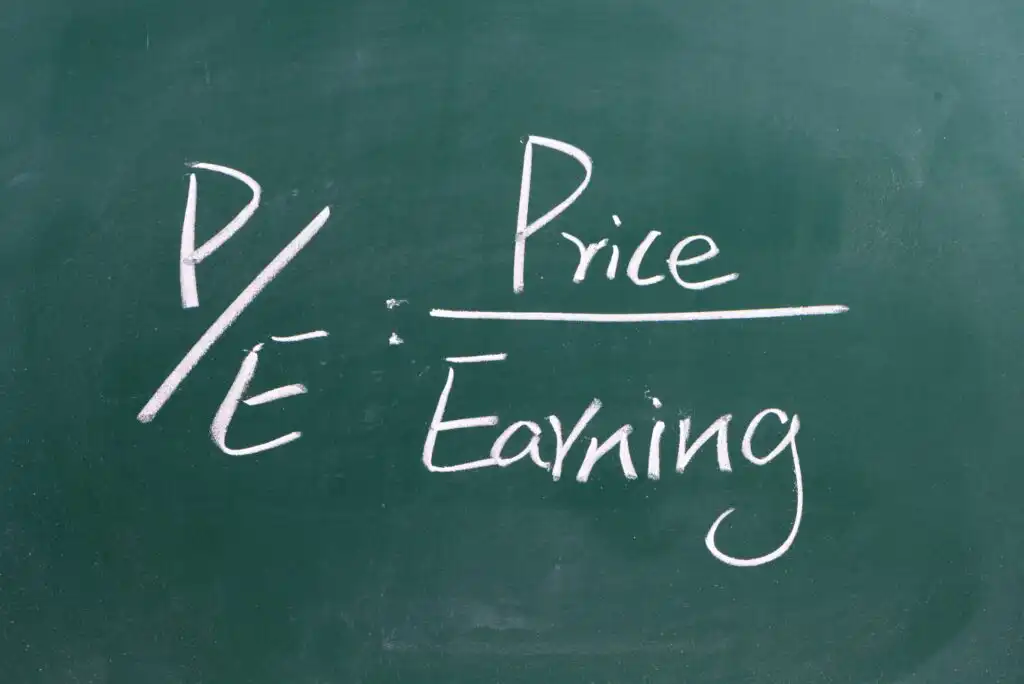 A chalkboard displays the formula P/E = Price / Earning written in white chalk, illustrating the price-to-earnings ratio used in financial analysis.
