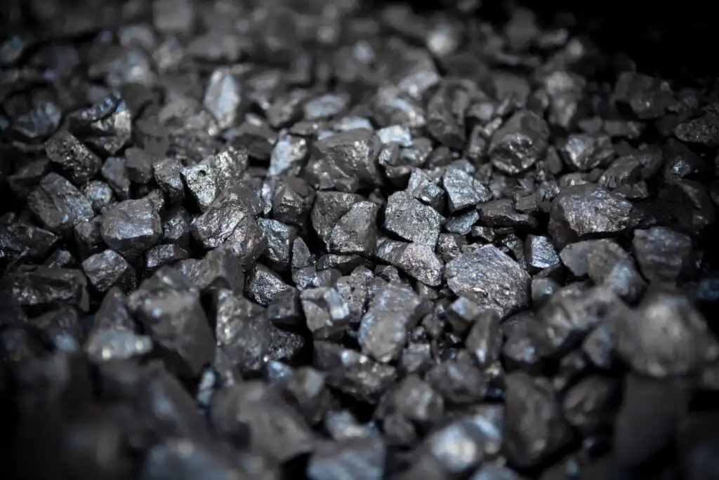 A close-up view of a pile of shiny black coal pieces, showing uneven, jagged surfaces and a metallic sheen under the light.