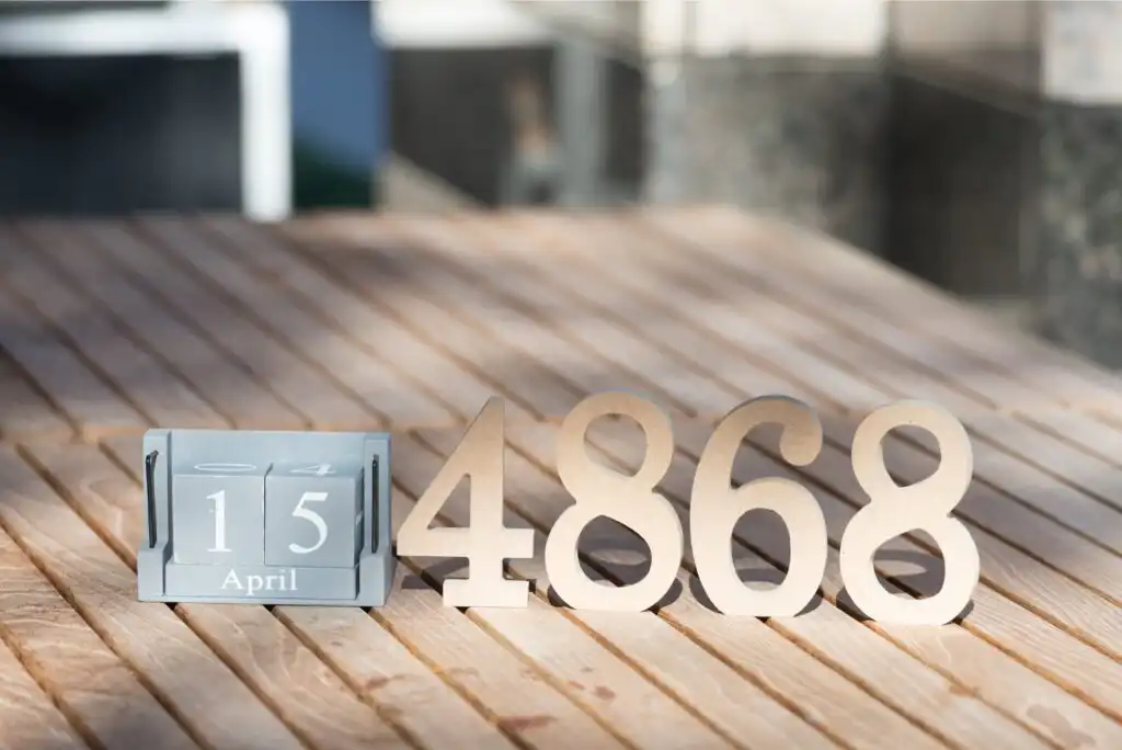 A desk calendar shows 15 April next to large wooden numbers 4868 on a wooden surface, with sunlight casting shadows across the scene.