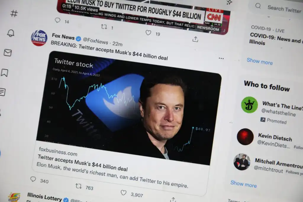A computer screen displays a tweet from Fox News about Elon Musks $44 billion deal to buy Twitter, with a photo of Musk, the Twitter logo, and a stock chart in the background.