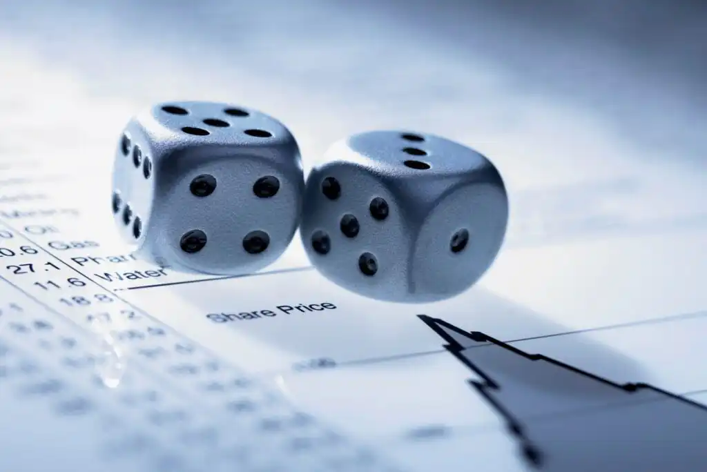 Two silver dice are placed on a financial document displaying numbers, text, and a declining stock price graph, symbolizing risk or chance in financial markets.