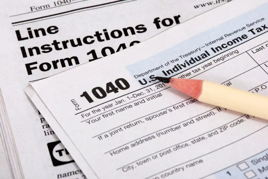 Close-up of a U.S. Individual Income Tax Return Form 1040 with a sharpened pencil resting on it and the instruction sheet partially visible in the background.