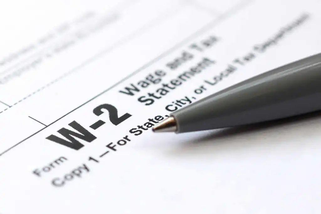 A close-up of a W-2 tax form with the label W-2 Wage and Tax Statement visible, and a gray pen resting on the paper.