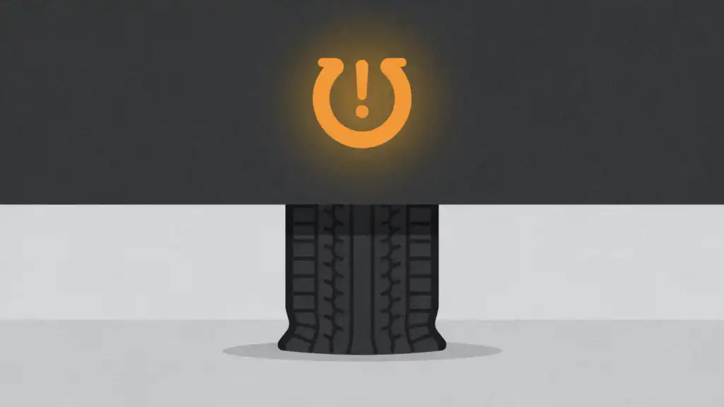 An amber tire pressure warning lamp glows above a black tire bulging low at its base on a pale grey floor.