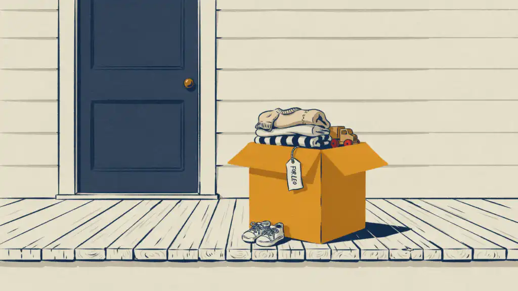 A mustard box of folded kids' clothes and a toy truck, tagged FOR LEO, beside small sneakers on a porch