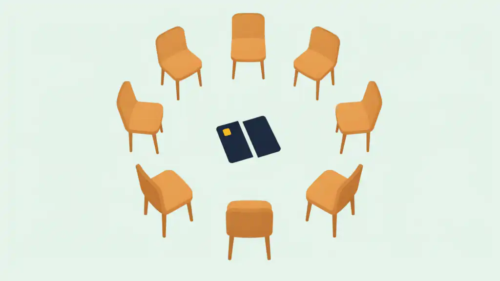 A circle of empty chairs around a credit card cut in half, set up like a support group for compulsive debting