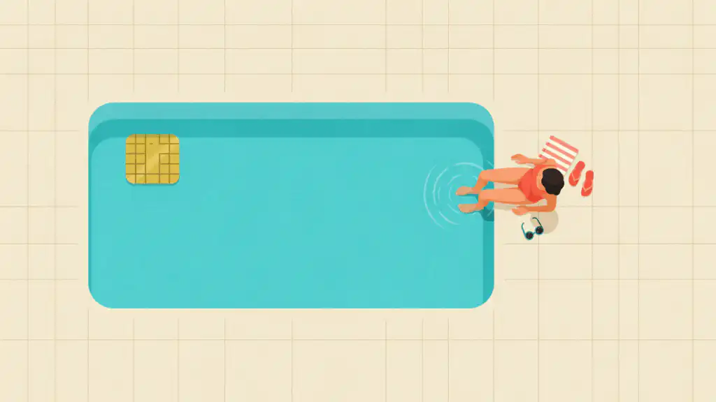 A person sits on the edge of a pool shaped like a credit card with both feet dipped in the water