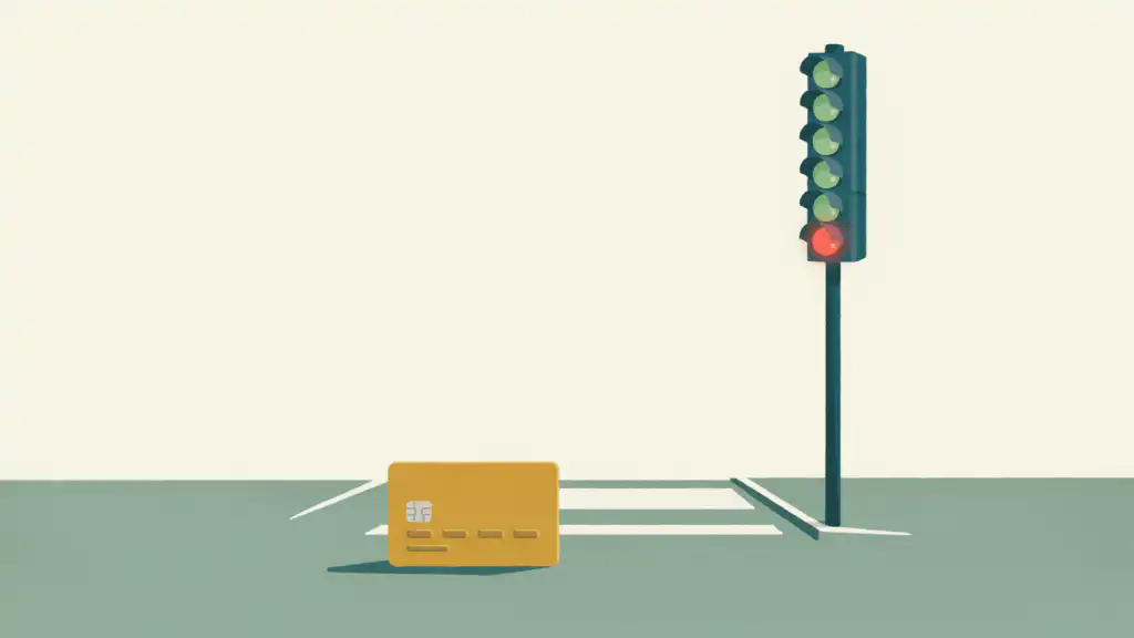 A gold credit card waits at a crosswalk beside a signal post with five green lamps and one red.