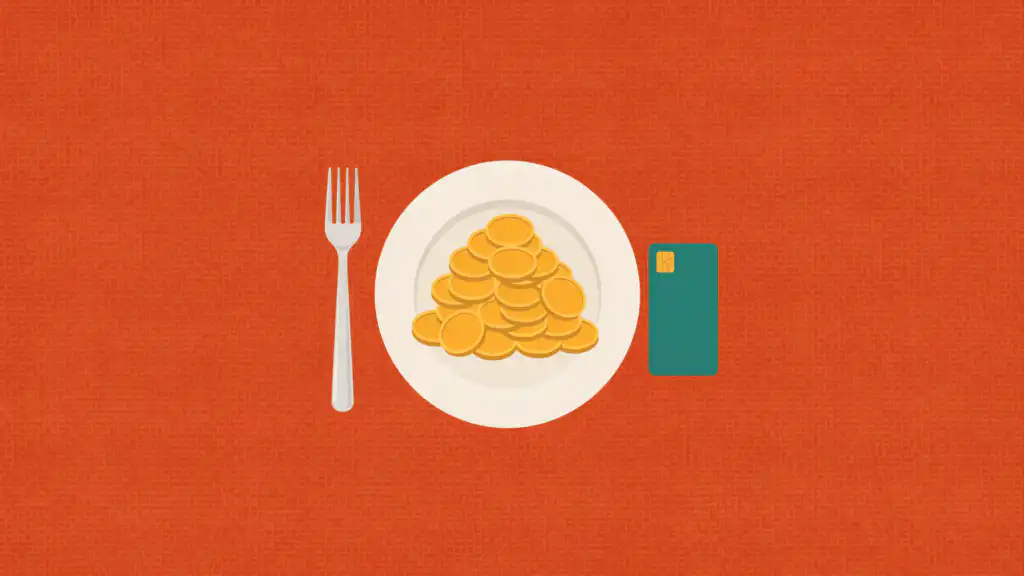 Dining credit card set beside a plate of gold coins and a silver fork on a terracotta tablecloth