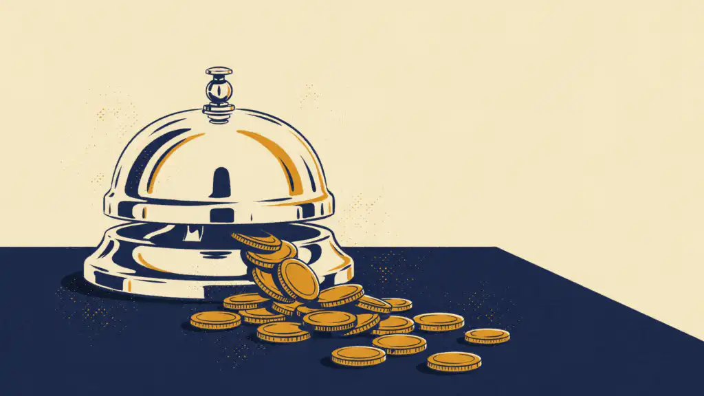 A silver hotel front desk bell on a navy counter with gold coins spilling out from under it toward the viewer