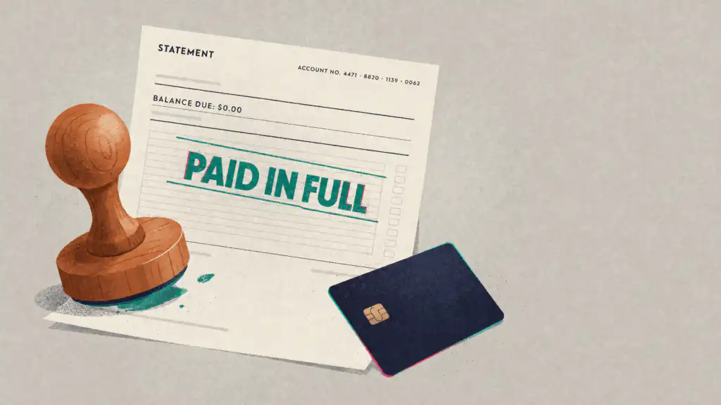 A wooden rubber stamp rests on a credit card statement stamped PAID IN FULL with $0.00 due, beside a navy credit card